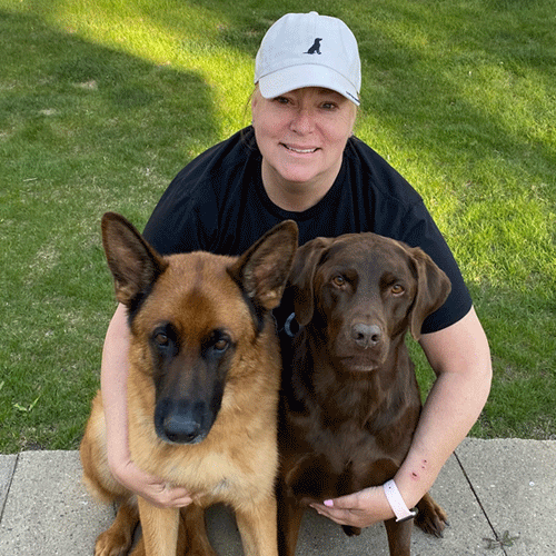 Calli, a Certified Dog Handler at The Chase, crouches with a German Shepherd and a chocolate lab.
