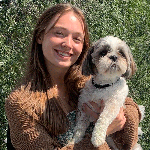 Avery, a Certified Dog Handler at The Chase, poses with a Shih Tzu outside on a sunny day.