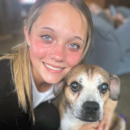 Faith, a Certified Dog Handler at The Chase, poses with a brown and white dog with a black nose.